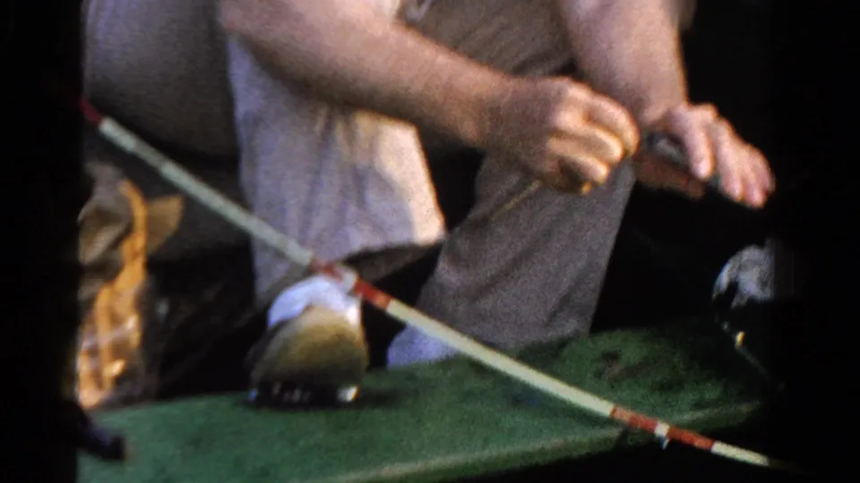 1958 Ontario home-movie frame showing a seated angler in light clothing working a fishing rod inside a small green boat.