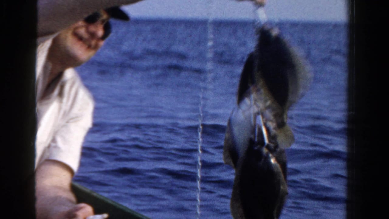 Older man in sunglasses on a boat in Ontario, Canada, holds several fish toward the camera in 1958 home-movie footage.