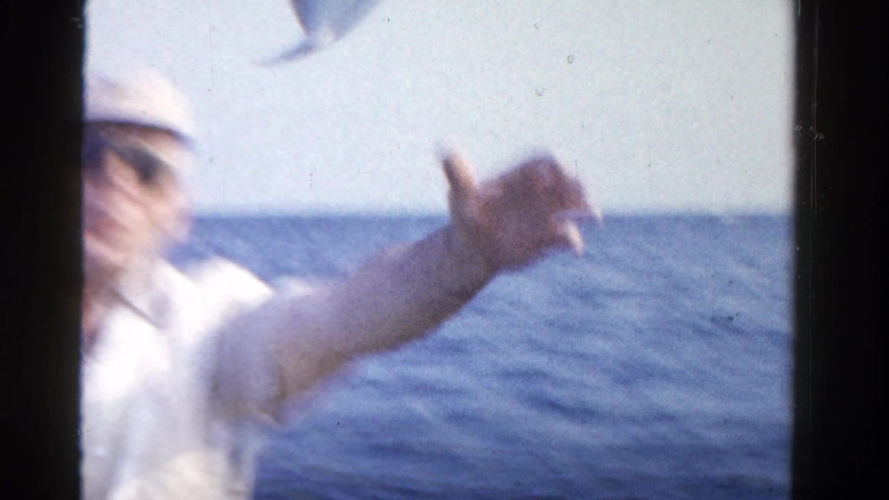 In a soft, overexposed 1958 Ontario boat scene, the man gestures near the camera with water and horizon behind him.