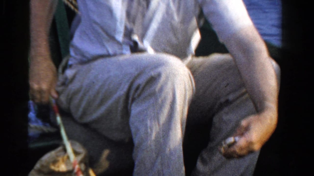 Seated man in light clothing holds fishing line inside a small boat.