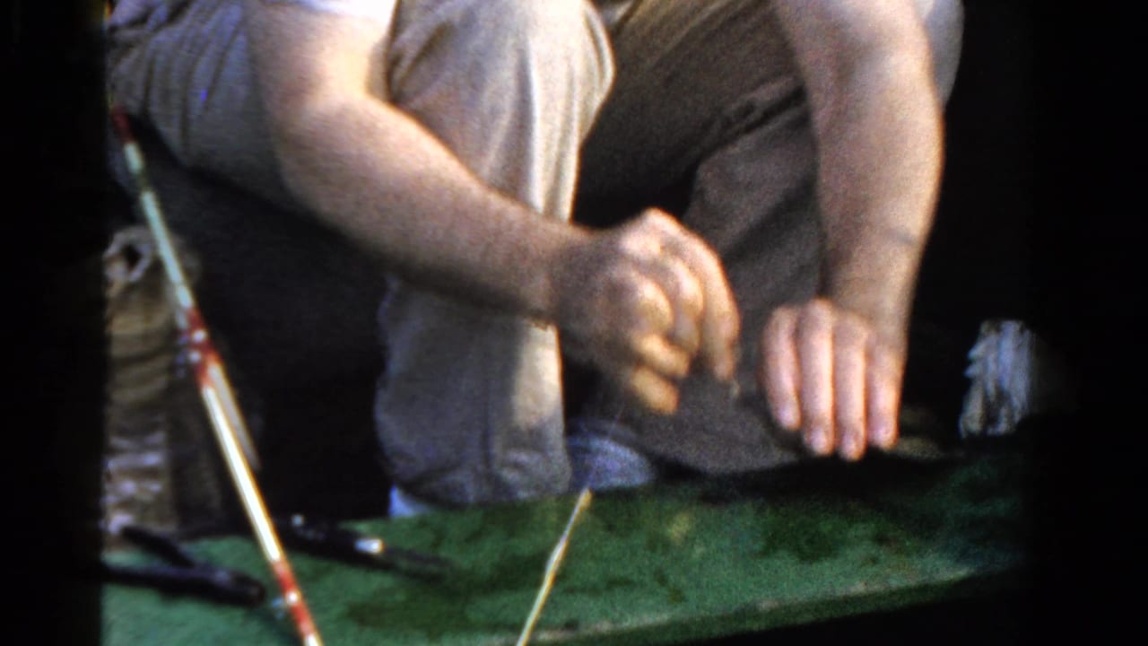 A man in a small Ontario boat leans over the green surface while handling fishing tackle in 1958 footage.