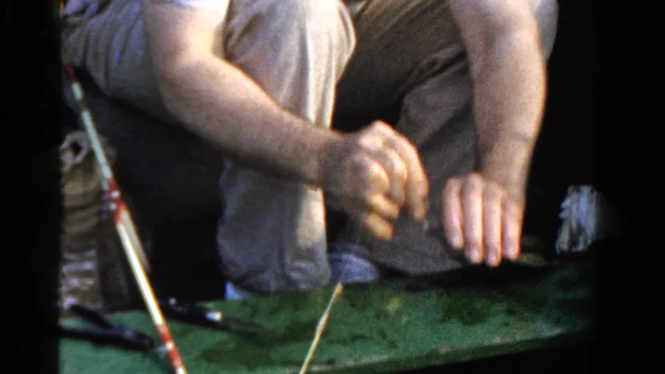A man in a small Ontario boat leans over the green surface while handling fishing tackle in 1958 footage.