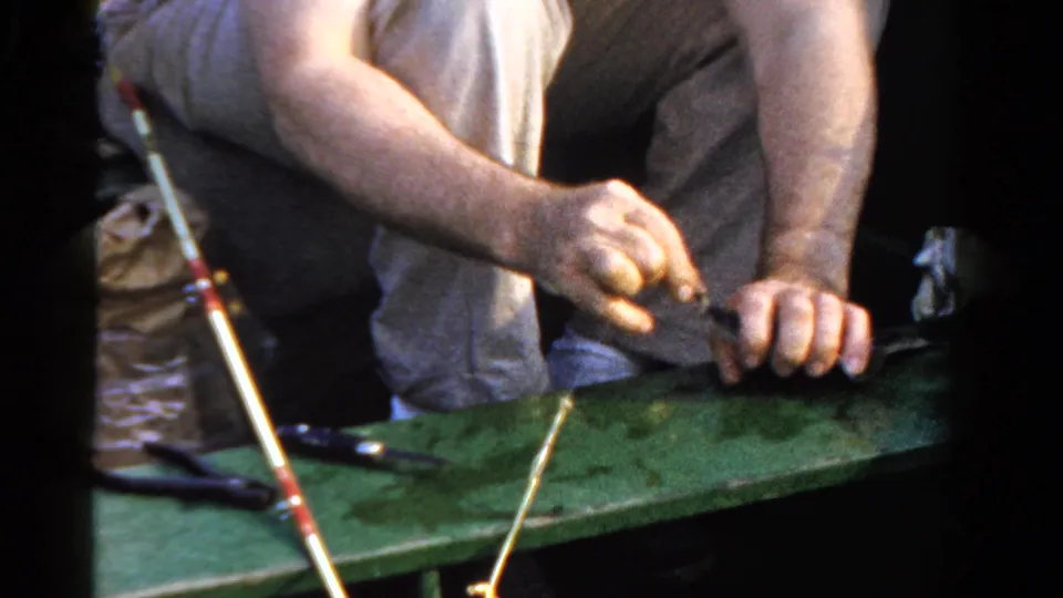 The home-movie frame shows the fisherman's hands working with line and tackle over a green boat surface.