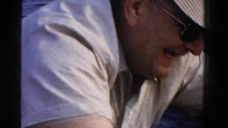 An adult man in sunglasses and a light shirt leans forward on a boat in Ontario, Canada, in 1958.