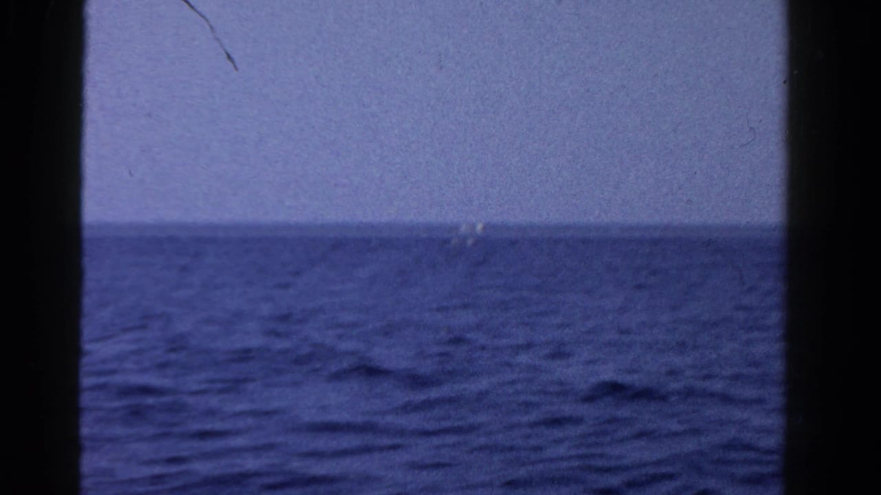 1958 Ontario 8mm view across blue water, with a tiny distant boat-like shape near the horizon.