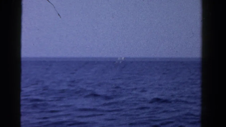 1958 Ontario 8mm view across blue water, with a tiny distant boat-like shape near the horizon.