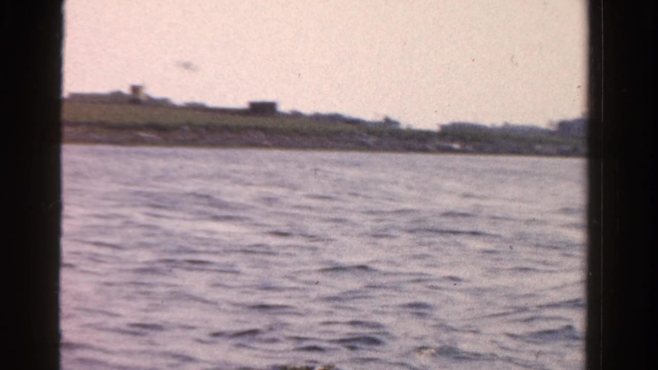 Rippling water seen from a boat with a low shoreline and dark window edges.