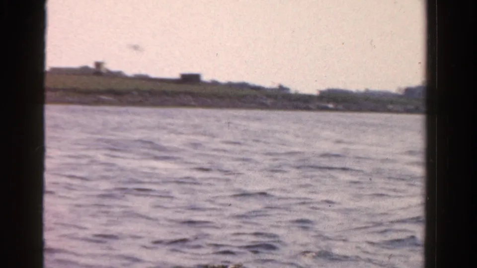 1958 Ontario 8mm boat view across rippling water toward a low distant shoreline, framed by dark vertical window edges.
