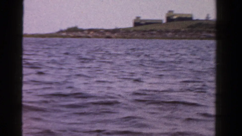 1958 Ontario home-movie view of choppy water with a low shoreline and a small building set back from the water.