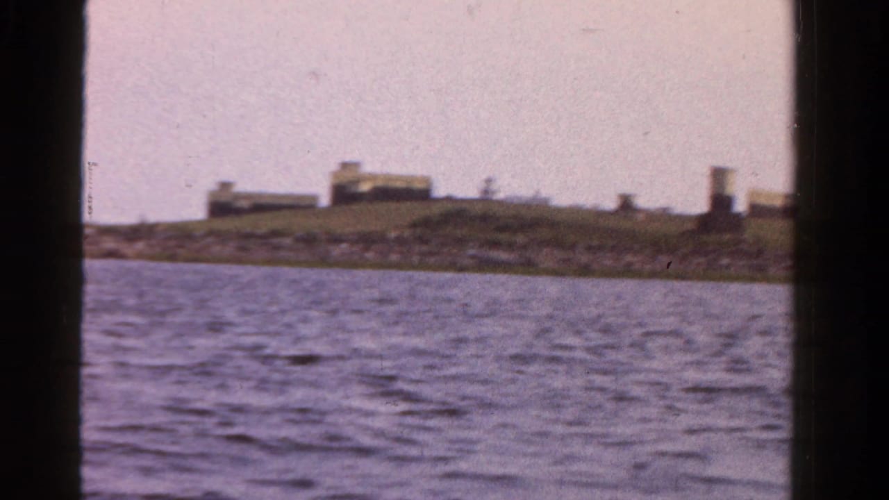 1958 Ontario home-movie frame with open water in the foreground and low shoreline buildings in the distance.