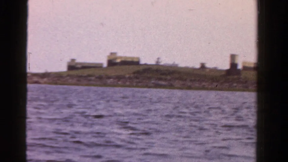 1958 Ontario home-movie frame with open water in the foreground and low shoreline buildings in the distance.