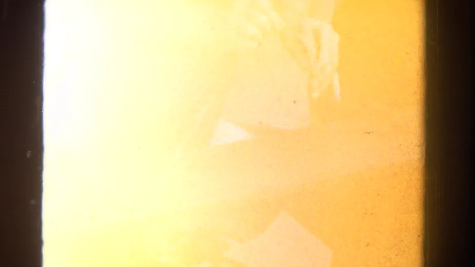 The final 8mm frame is heavily overexposed, with a faint seated figure and warm yellow flare from the film scan.