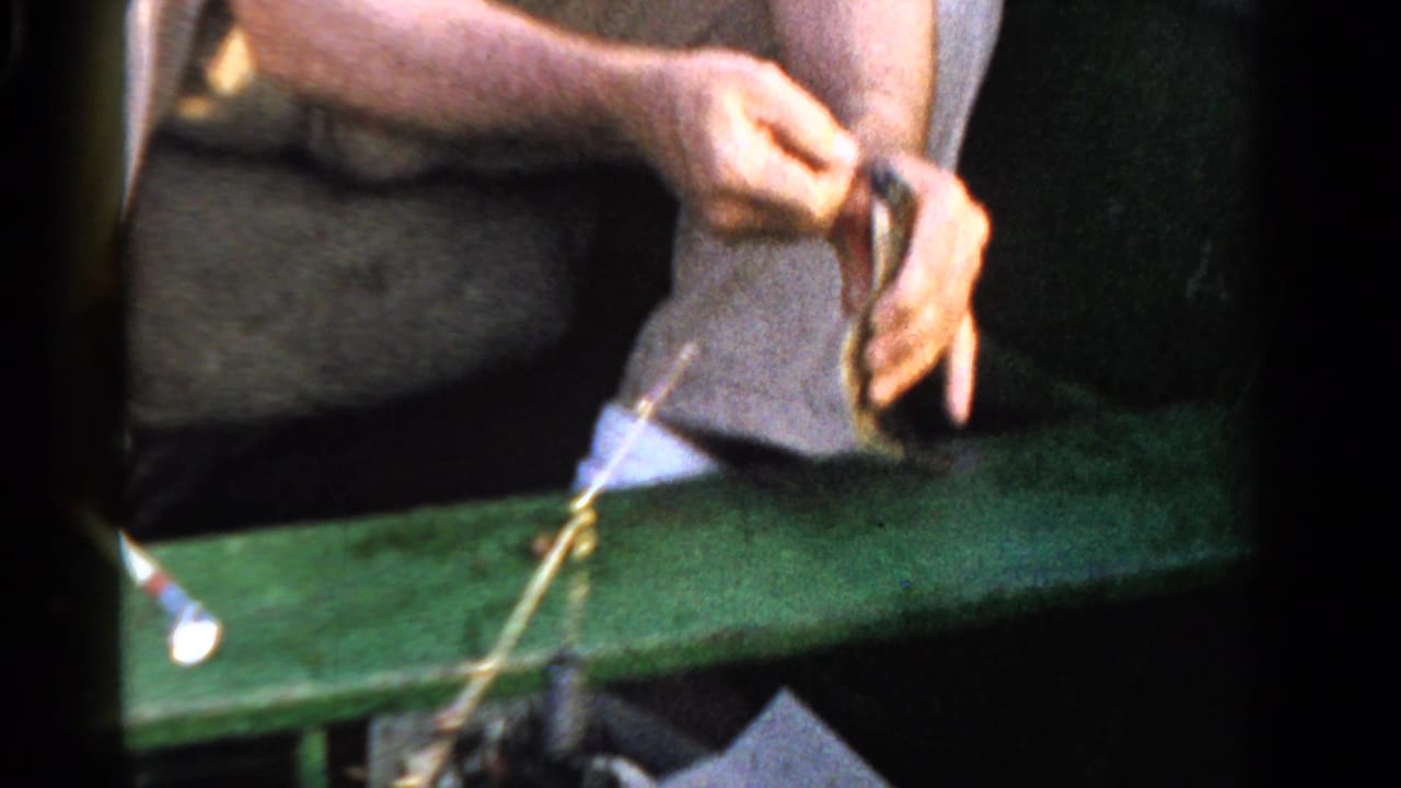 In Ontario, Canada in 1958, a man in light clothing sits in a green boat while handling a small fish and fishing line.