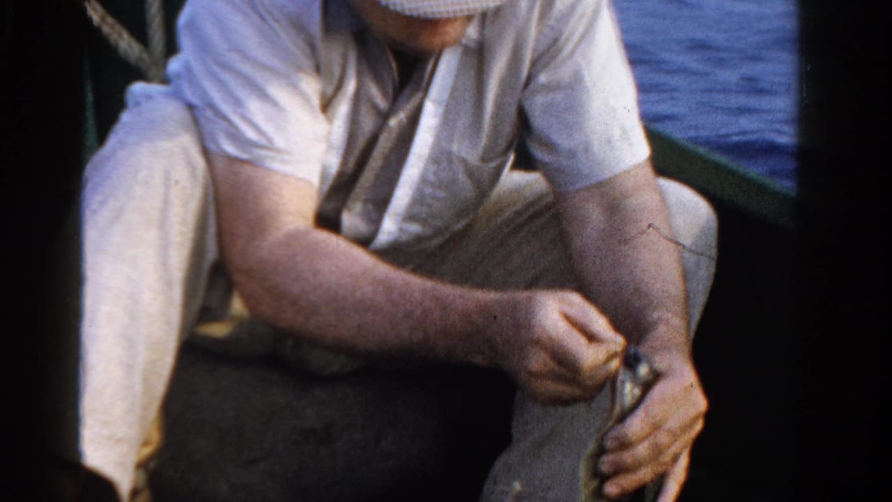 In the 1958 Ontario home-movie frame, the seated man holds a small fish close to his knee while working near the hook.