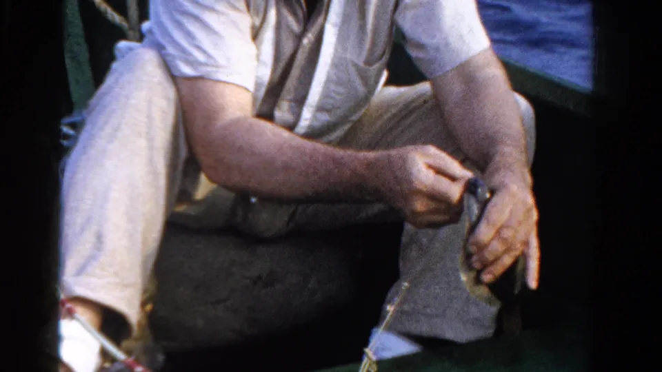 The Ontario fishing scene shows the seated man in light clothing holding the small fish steady inside the green boat.