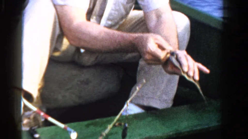 At the end of the 1958 Ontario clip, the man extends the small fish and line near a rod resting across the green boat.