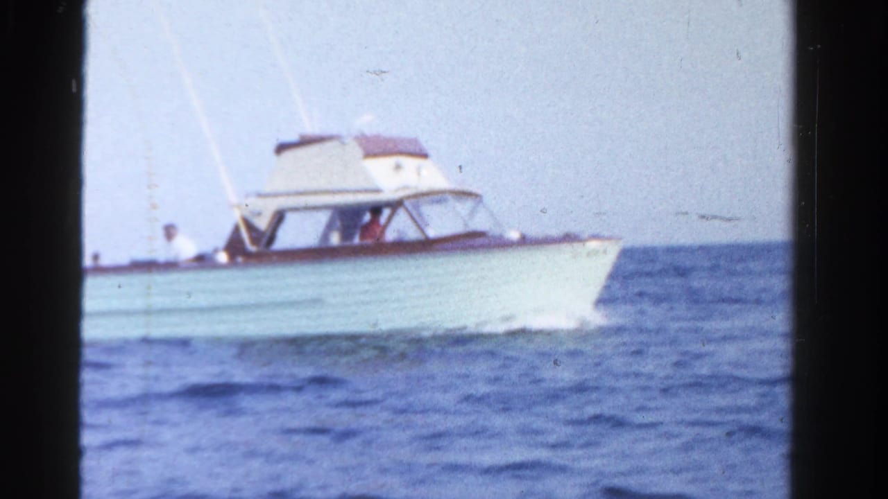 A white mid-century motor yacht with wood trim moves across open water in the Ontario 1958 footage.