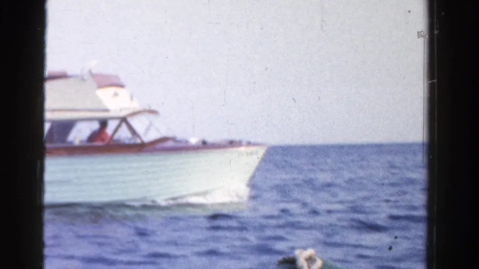 A white motor yacht with wood-framed cabin details cruises over small waves in the 1958 Ontario home-movie scene.