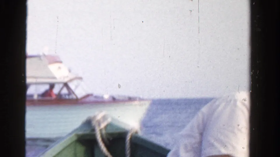 1958 Ontario home-movie frame showing a light motorboat near a green rowboat on lake water.