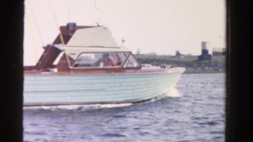 1958 Ontario home-movie view of a light wooden-trim motorboat traveling along the lake near a low shoreline.