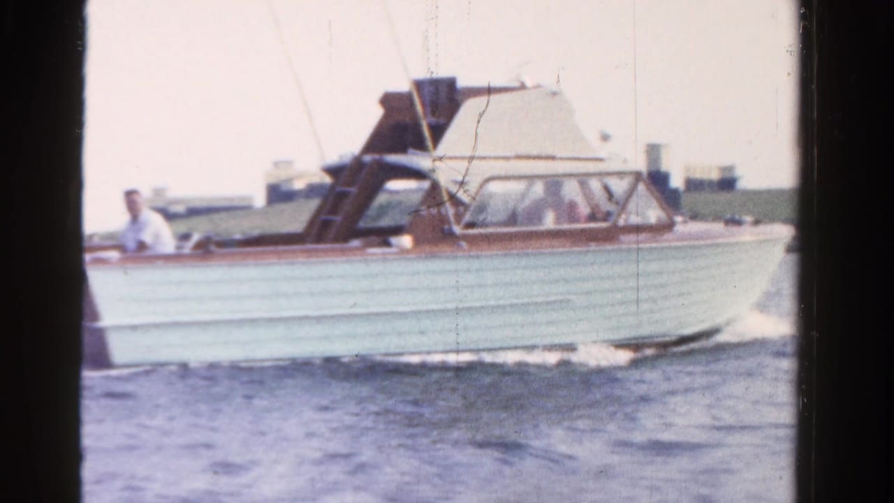 1958 Ontario 8mm frame showing a light blue and brown motorboat crossing calm water with a man aboard.