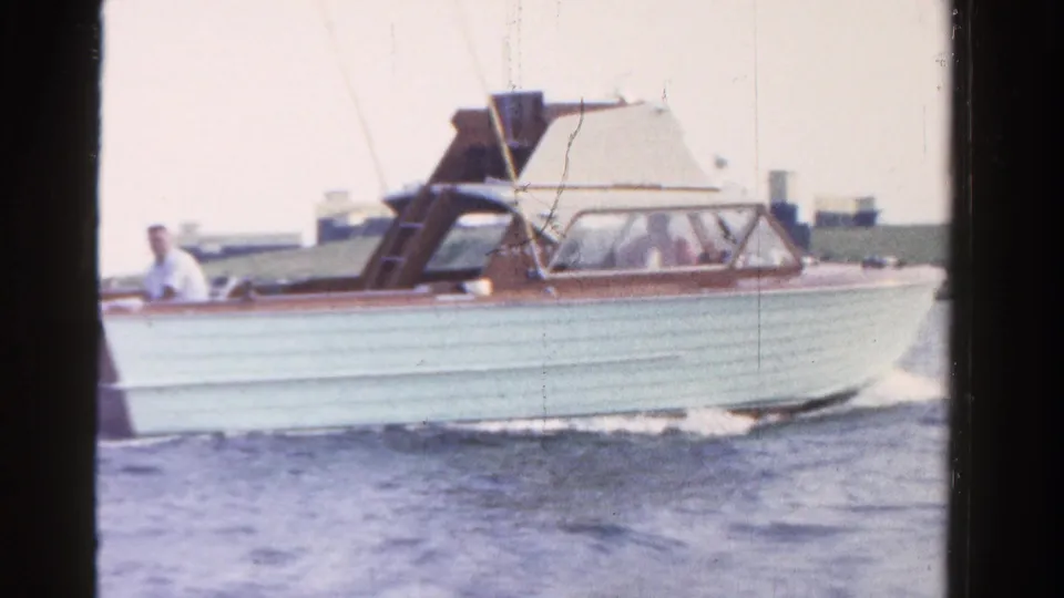 1958 Ontario 8mm frame showing a light blue and brown motorboat crossing calm water with a man aboard.