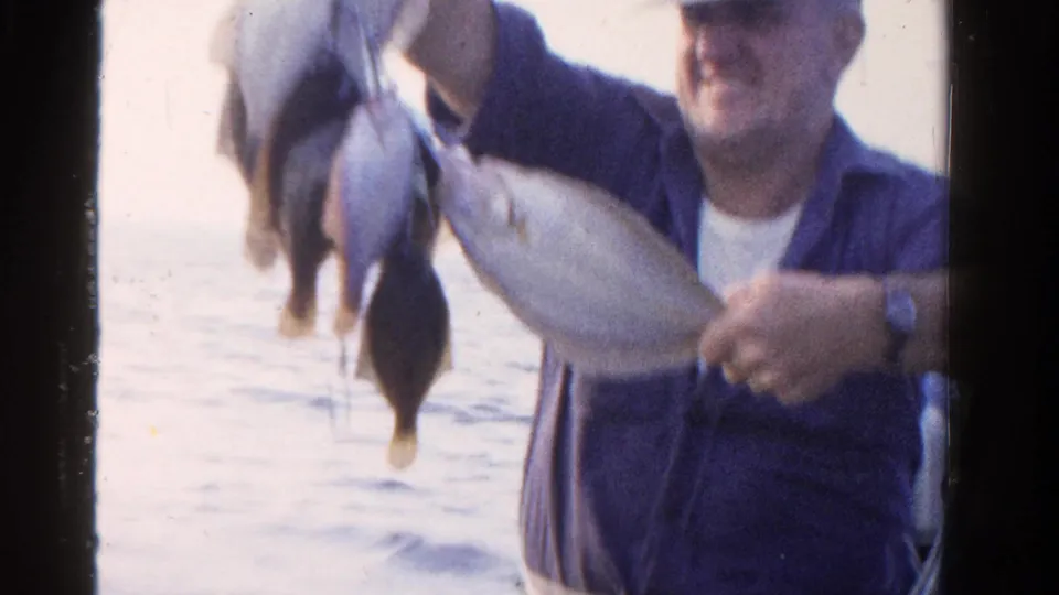 The 8mm frame shows the fisherman holding the catch closer to the lens, with fish dominating the foreground and water behind.