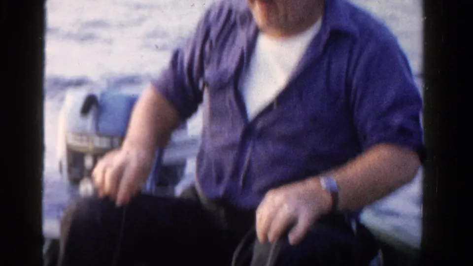 Older man in a purple shirt sits in a small boat on Ontario water in 1958, partly cropped beside an outboard motor.