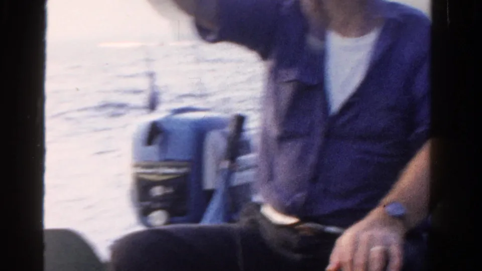 The man leans forward in the boat, with lake water and an outboard motor visible behind him in the 1958 Ontario footage.