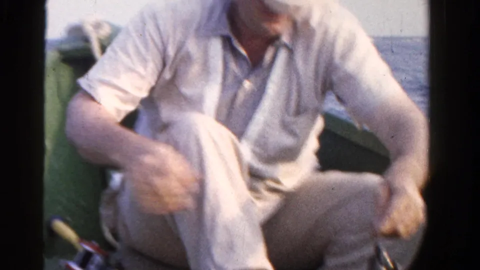 The adult fisherman sits relaxed in the small green boat with fishing gear nearby and Ontario water behind him.
