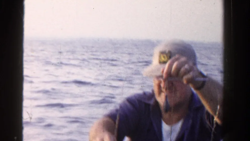 In the 1958 Ontario fishing clip, a man in a cap raises a small fish on a line toward the camera on the open lake.