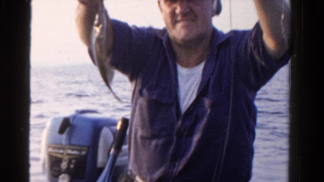 Man on a boat holds up a fish beside open water and an outboard motor.
