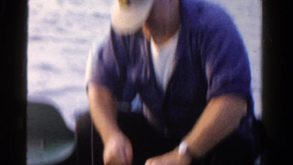 A soft, motion-blurred 8mm frame shows the seated fisherman leaning forward on the boat as water fills the background.