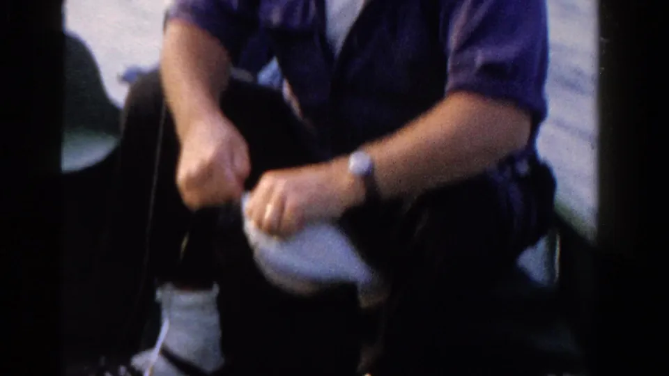 The fisherman holds a small fish close to his lap while seated in the boat, continuing the hook-removal moment in 1958 Ontario footage.
