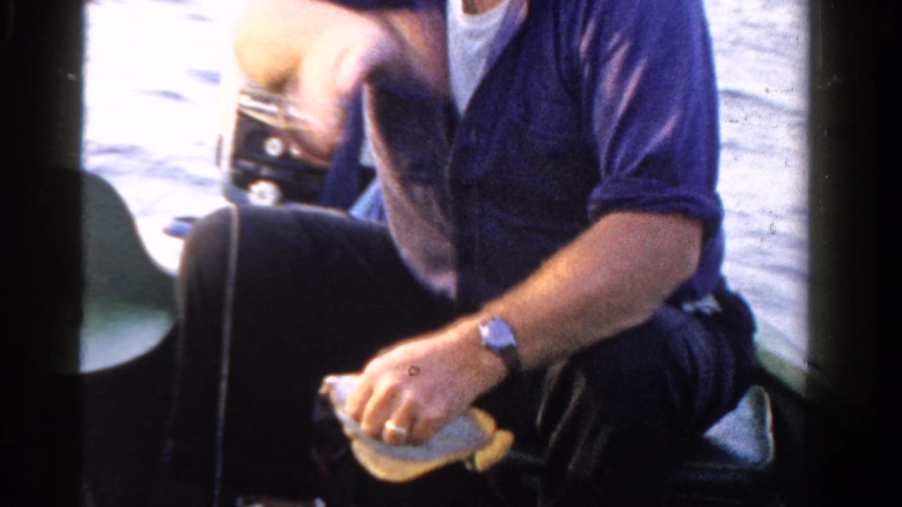 In 1958 Ontario home-movie footage, a man in a white cap and purple shirt sits in a boat while handling a fish.