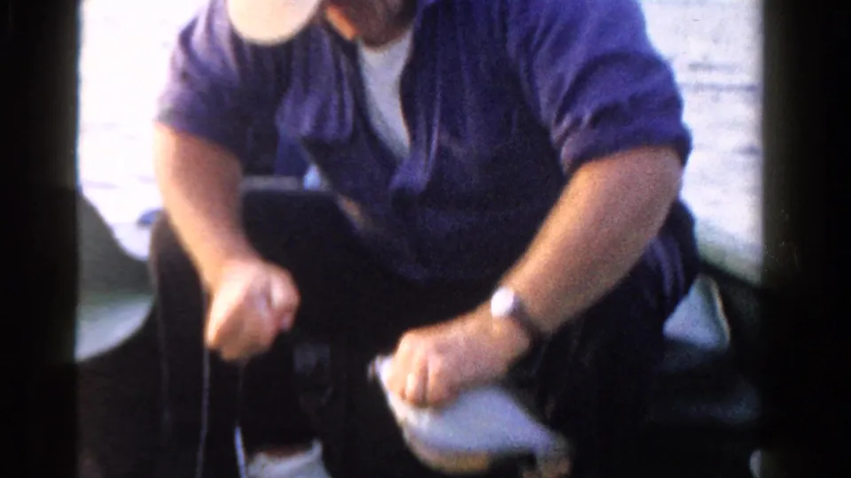 A blurred 8mm frame shows the man leaning forward in the boat, holding the pale fish near his knee.