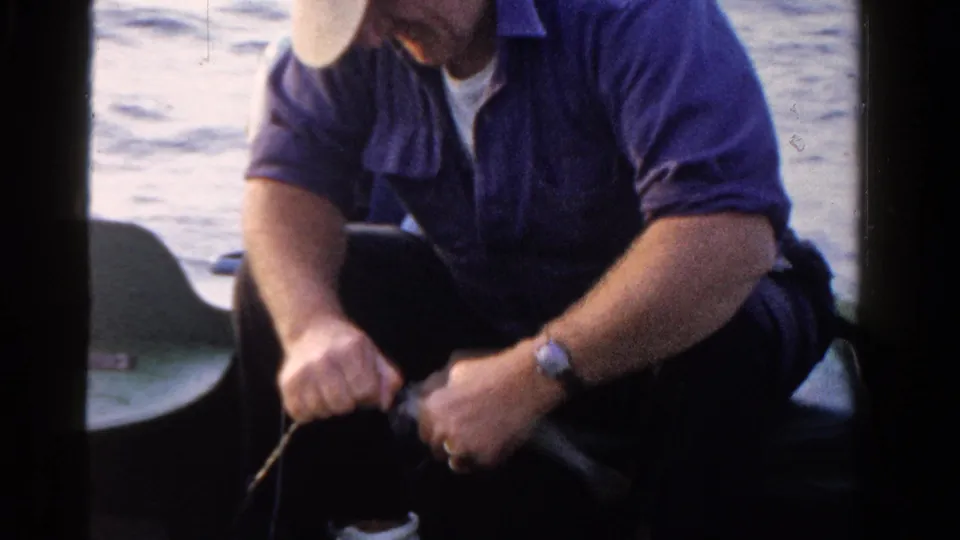 The man remains seated on the boat in Ontario, Canada, handling a fishing line or bait with lake water in the background.