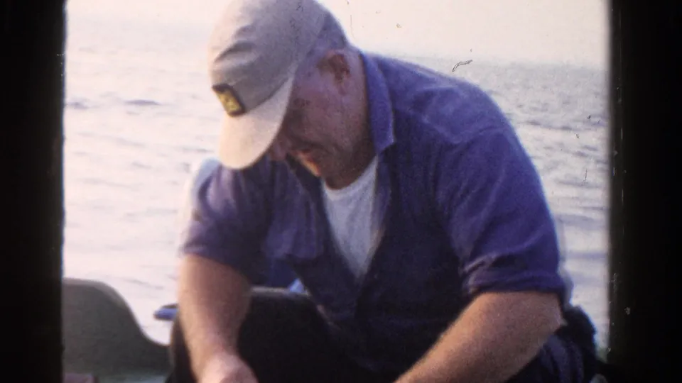 The final frame shows the man seated low in the small boat, cap brim down, with Ontario lake water and a faint horizon behind him.