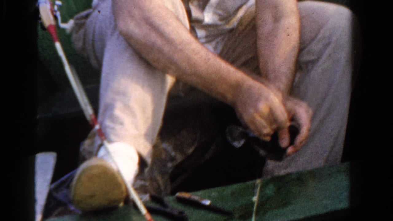1958 Ontario home-movie frame showing a seated fisherman in light clothing working with a small fish and line inside a boat.