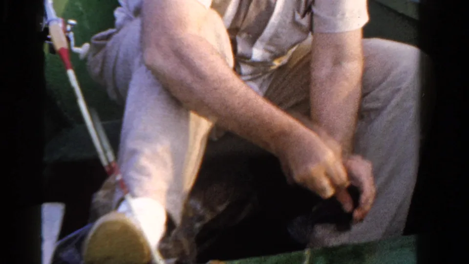 Close 8mm view of a fisherman in Ontario handling a small fish and tackle from a seated position in the boat.