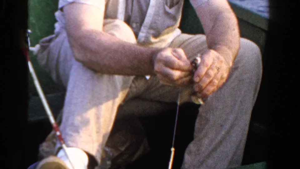 1958 Ontario fishing footage frame with the fisherman gripping the fish and line while seated in the small boat.