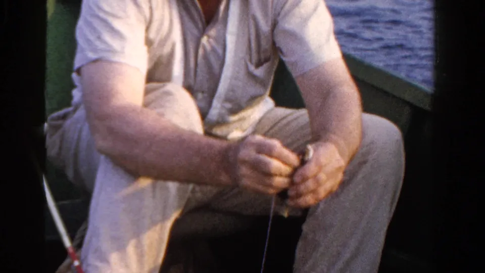 Final 8mm frame of the Ontario fisherman holding the small fish in his lap area, with open water behind the boat.