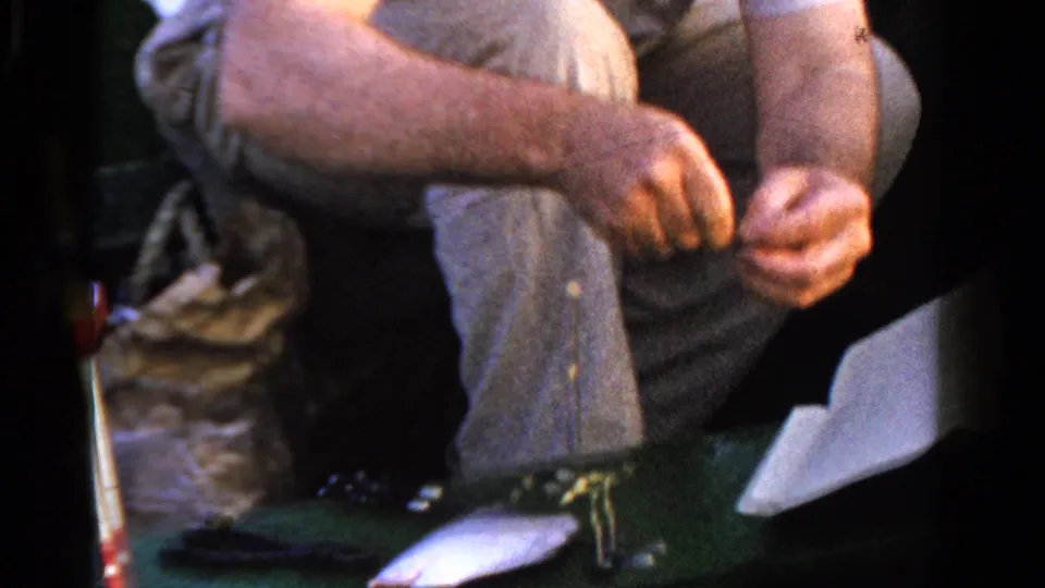 The 1958 Ontario fishing footage shows a seated man handling gear while a small fish lies on the green boat floor near rods and tackle.
