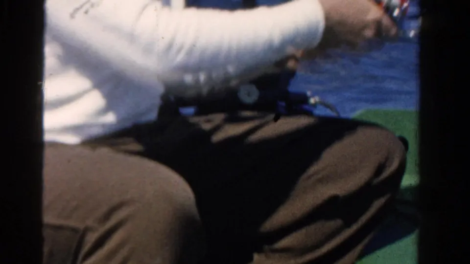 Close 8mm frame of an adult's hands working a fishing reel from a small boat during the 1958 Ontario outing.