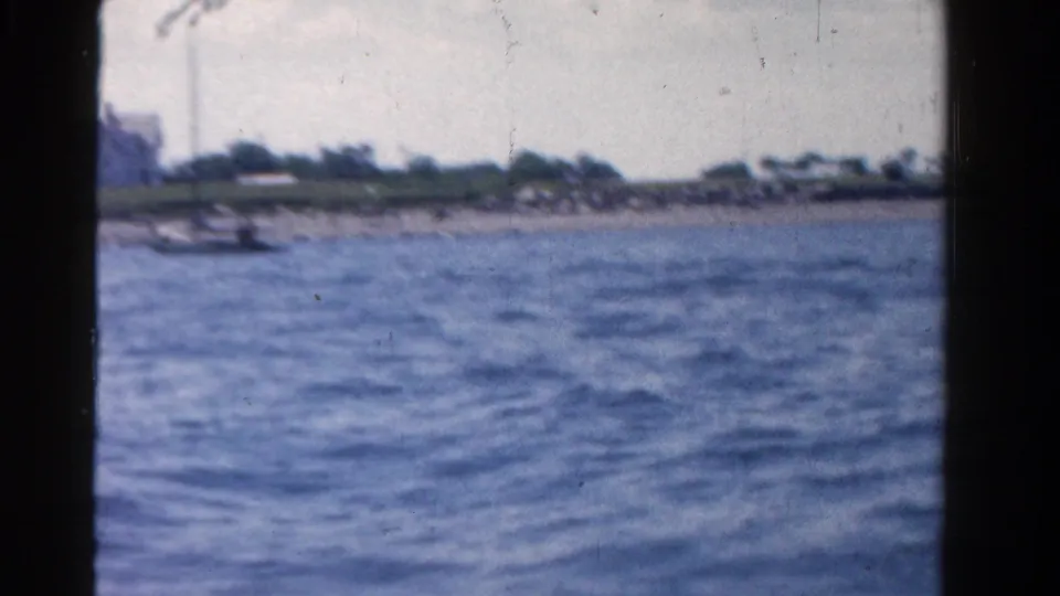 1958 Ontario 8mm frame with the camera drifting past a low shoreline, small boat, and wind-textured lake surface.