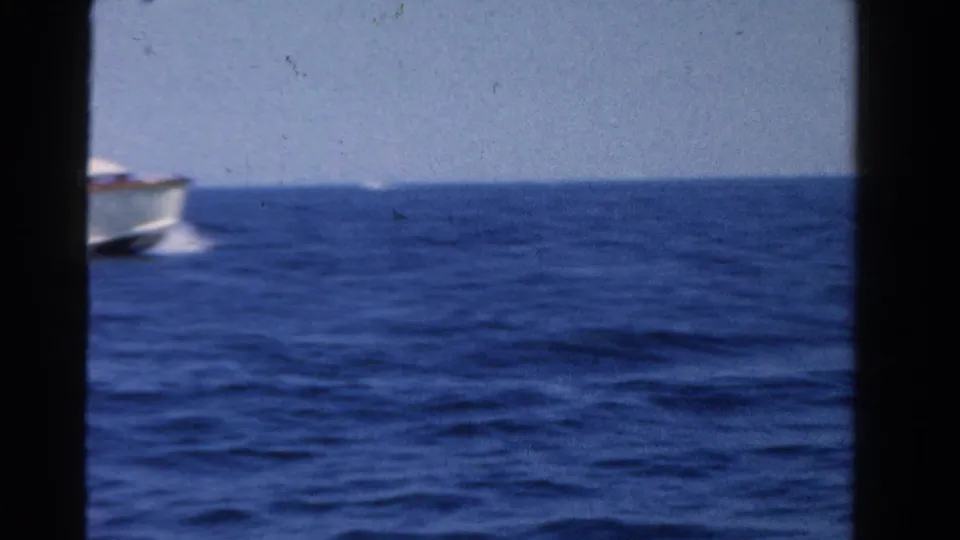 1958 Ontario 8mm frame showing open blue lake water, a partial passing boat, and a distant horizon under a pale sky.