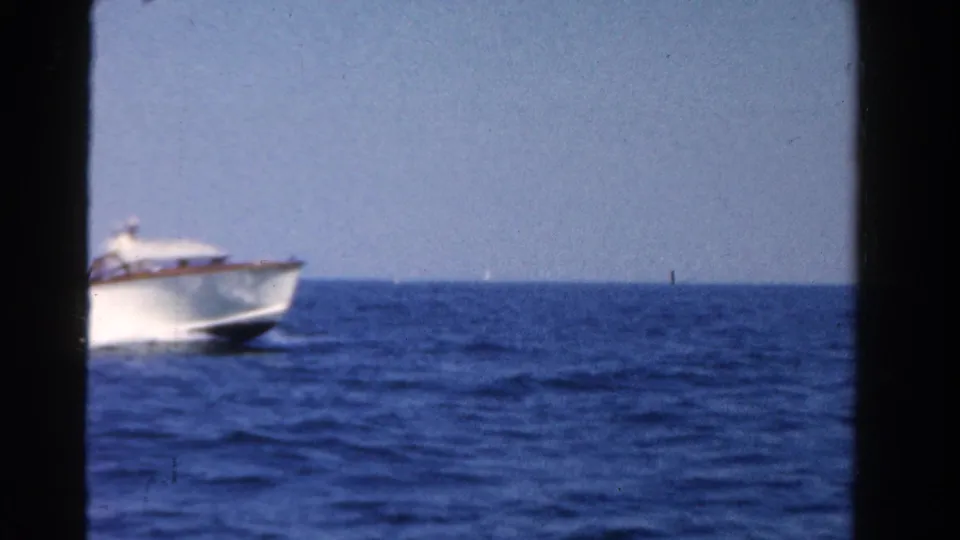1958 Ontario home-movie frame with a white speedboat partly visible at left on open blue water beneath a clear bright sky.