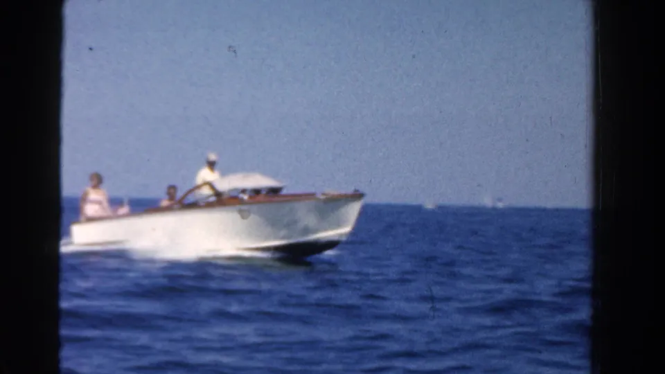 1958 Ontario 8mm frame showing a white speedboat with a capped driver and passengers moving across open blue water.
