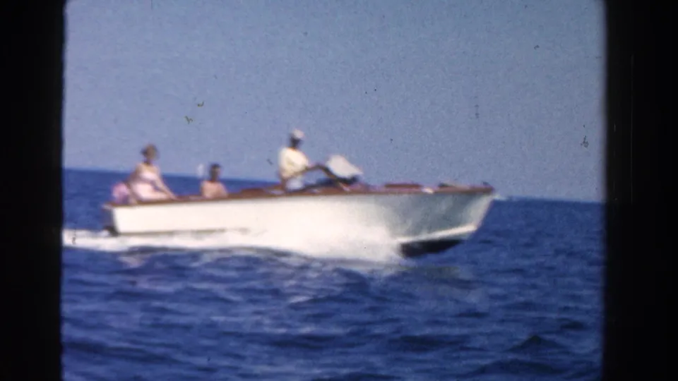 1958 Ontario frame showing a white speedboat carrying several people across blue water, leaving a visible wake behind it.