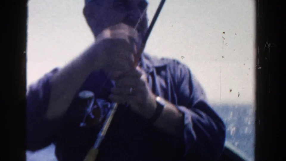 A man in a cap handles a fishing rod on or near a boat, with open water behind him in the 1958 Ontario footage.